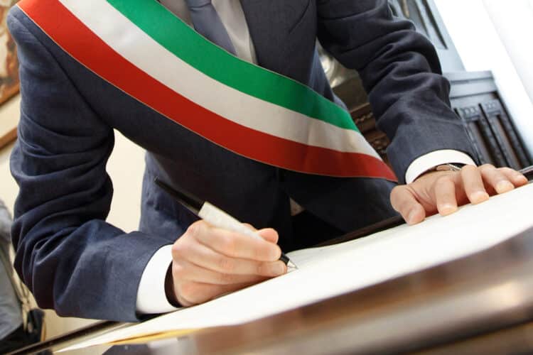 foto b/n della mano di un sindaco con fascia tricolore che firma